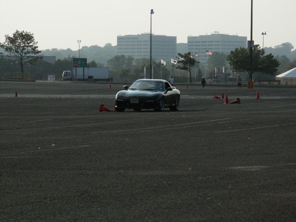 Black sports car on asphalt with orange cones, buildings in background
