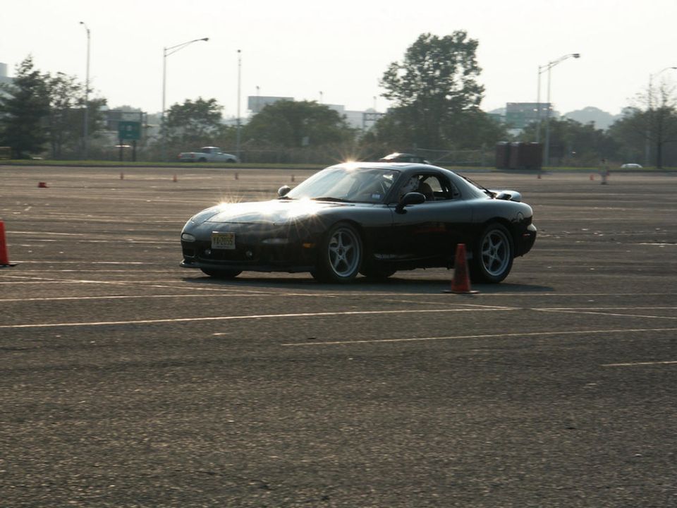 Black sports car on asphalt with orange cones, sun glare on windshield