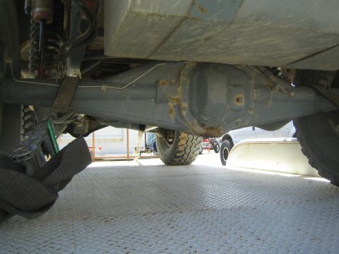 1990 Ford Bronco - Under-vehicle view of an off-road truck's rear axle, differential and coilover shock with a tie-down strap on a trailer deck.