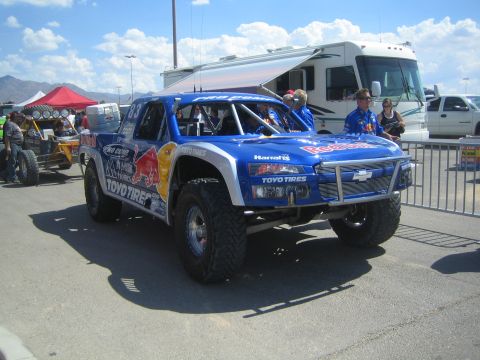 1990 Ford Bronco - blue Red Bull and Toyo Tires Chevrolet trophy truck sits in a paved pit area with crew, spectators and a motorhome behind.