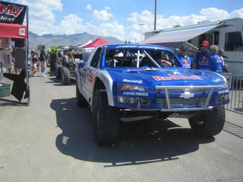 1990 Ford Bronco - Front view of a blue Red Bull and Toyo Tires Chevrolet trophy truck staged in a pit lane with crew in matching shirts.