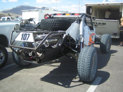 1990 Ford Bronco - white tube-chassis off-road race buggy marked 107 sits in a parking lot, rear engine and dual spare tires exposed.
