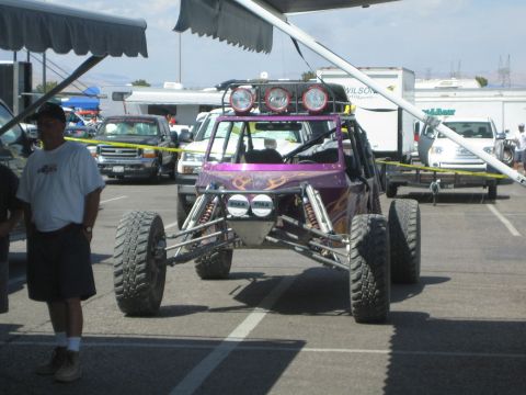 1990 Ford Bronco - purple off-road race buggy with flame graphics and a four-light roof bar sits under a canopy as a man walks past.