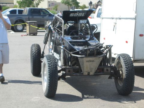 1990 Ford Bronco - black single-seat tube-chassis off-road race buggy numbered 1609 parked on pavement next to a white trailer.
