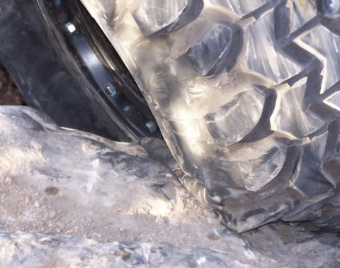 1981 Ford Bronco - Off-road tire tread detail pressed against rocks, with visible rim bolts.