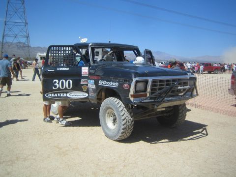 1990 Ford Bronco - black Ford pickup race truck numbered 300 with Deaver Suspension and BFGoodrich graphics sits in a dusty desert.