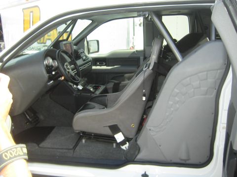 1990 Ford Bronco - stripped interior of a race vehicle with a gray suede racing seat, roll cage and small steering wheel.