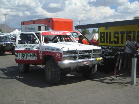 1990 Ford Bronco - white-and-red California Tomatoes off-road race truck parked next to a yellow Bilstein racing shock display.