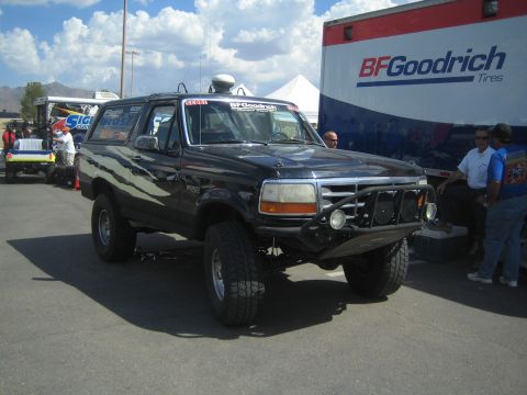 1990 Ford Bronco - black full-size Ford Bronco off-road race truck with tube bumper parked before a BFGoodrich Tires hauler.