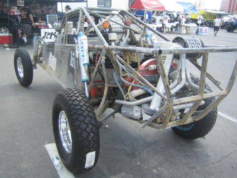 1990 Ford Bronco - Rear three-quarter view of a tube-frame off-road race buggy number 1616 with an exposed engine and exhaust, parked in a busy pit area.