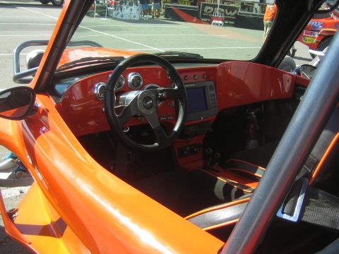 1990 Ford Bronco - Cockpit of an orange off-road buggy with a three-spoke steering wheel, round gauges, a digital display and a body-color dashboard.