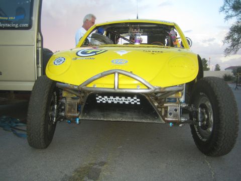 1990 Ford Bronco - Head-on view of a yellow VW Beetle-bodied Baja race car with a tube front bumper and large off-road tires, with people standing behind it a…