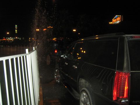 1990 Ford Bronco - black SUV parked at night behind a white fence with a lit casino sign in the distance.