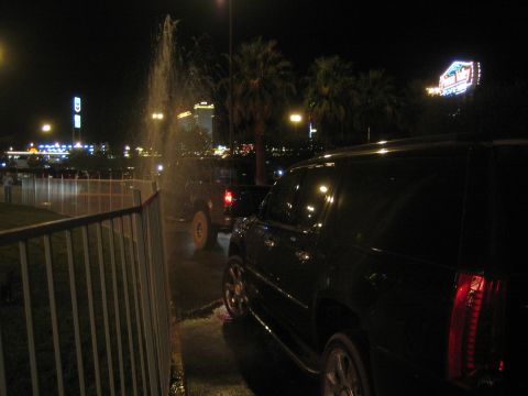 1990 Ford Bronco - black SUV parked at night near a fence and palm trees with distant city and casino lights.