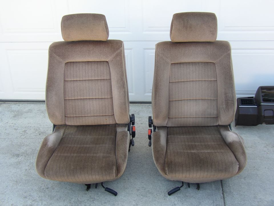 Pair of tan cloth bucket seats with headrests set on a driveway by a garage door