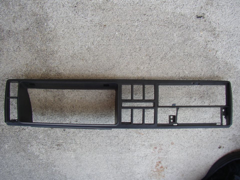 Black plastic dashboard trim piece with openings for radio and vents