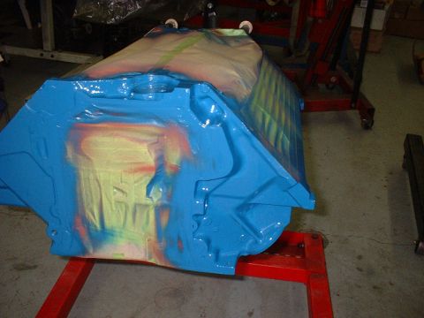 1969 Ford Mustang - An engine block is partially covered in blue paint and masking tape while on a red stand.