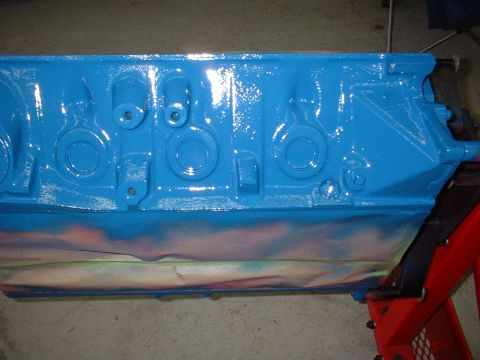 1969 Ford Mustang - A blue painted engine block rests on red jack stands, showing signs of recent spray painting with overspray on the lower section.