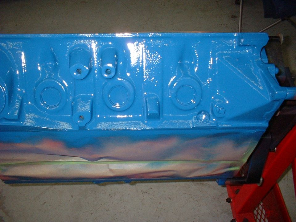 Blue painted engine block on red jack stands, with masking tape and spray paint overspray on the bottom