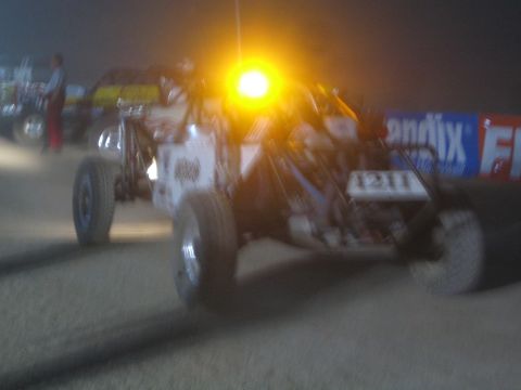 1990 Ford Bronco - open tube-frame number 1211 off-road race buggy with an amber roof beacon on a dirt course at night.