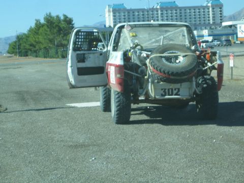 1990 Ford Bronco - Rear view of a stripped red-and-white off-road race truck marked 302 with a spare tire and open door, parked on pavement.