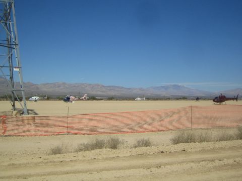 1990 Ford Bronco - Several helicopters sit parked on a desert flat behind an orange safety fence with mountains under a clear blue sky.