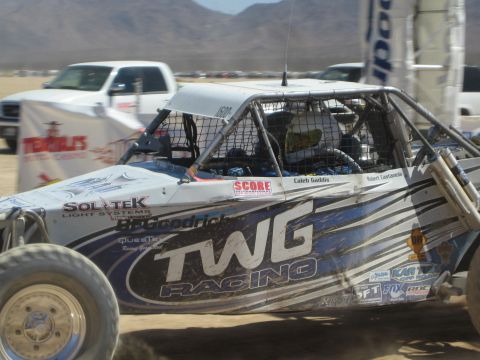 1990 Ford Bronco - Side view of a blue tube-frame off-road buggy with TWG Racing livery and a caged cockpit on a dusty desert course.