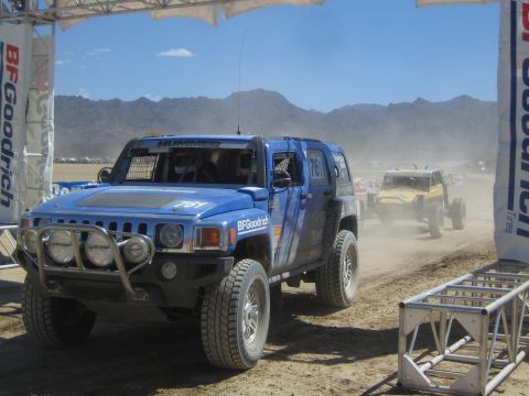 1990 Ford Bronco - blue Hummer H3 off-road race truck numbered 761 with sponsor graphics passes a BFGoodrich arch on a dusty desert course.