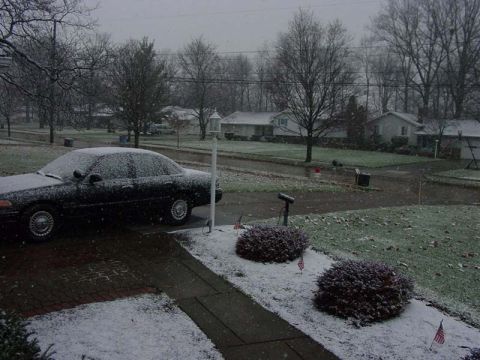 1999 Ford Crown Victoria - A black sedan sits covered in snow on a winter day, with houses and bare trees in the background.