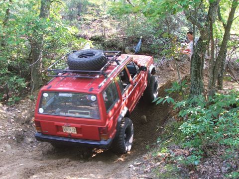 1996 Ford Bronco - Red Jeep Cherokee navigates a challenging off-road trail with a spare tire mounted on the roof rack.