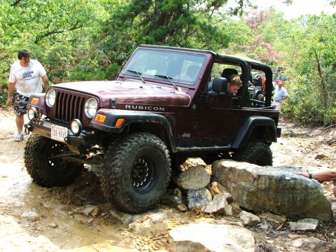 1996 Ford Bronco - A maroon Jeep Wrangler Rubicon navigates a rocky trail with people around.