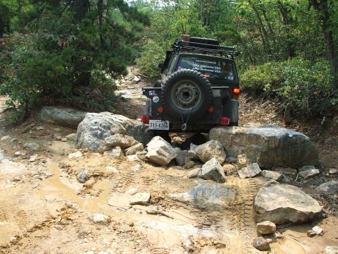 1996 Ford Bronco - This off-road vehicle is carefully maneuvering over large rocks on a muddy trail.