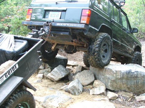1996 Ford Bronco - A green Jeep Cherokee XJ navigates a rocky trail while towing a trailer.