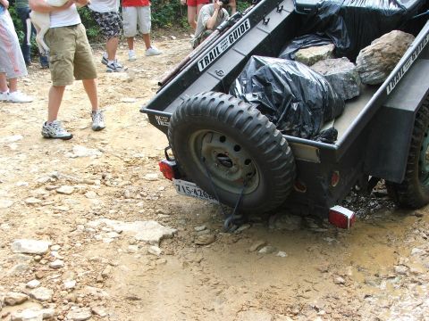 1996 Ford Bronco - A trailer is loaded with rocks and a spare tire, parked on a muddy dirt road.