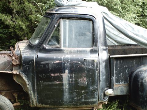 1955 Ford F-100 - Side view of a weathered 1955 Ford F-100 pickup truck with a tarp over the bed.