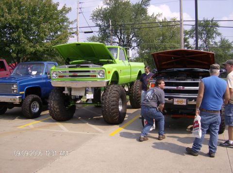 1970 Ford Ranchero - Three lifted pickup trucks are parked together, with two of their hoods open, as people look on.