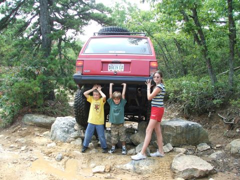 1996 Ford Bronco - Three children pose with a red Jeep Cherokee as it navigates an off-road trail.
