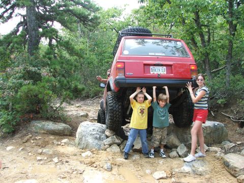 1996 Ford Bronco - Kids pose under a lifted Jeep Cherokee XJ on a rocky trail.