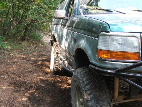 1996 Ford Bronco - The front passenger side of a green 1996 Ford Bronco is shown on a dirt path surrounded by trees.