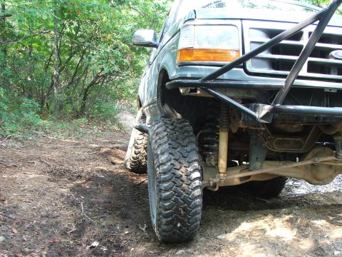 1996 Ford Bronco - A modified Ford Bronco navigates a wooded trail with its front wheel angled towards the camera.