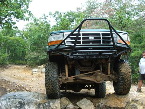 1996 Ford Bronco - A green 1996 Ford Bronco navigates a rocky trail, its off-road capabilities with a custom bumper and roll cage.