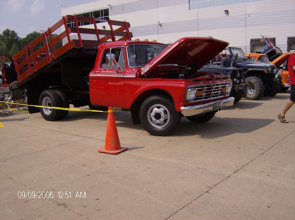Red flatbed truck with hood open, parked in a line with other vehicles