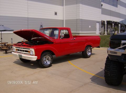 1970 Ford Ranchero - A red pickup truck from the mid-1960s is shown with its hood open, parked outdoors next to another vehicle.