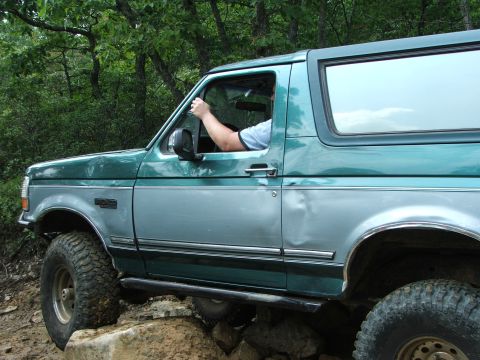 1996 Ford Bronco - A 1996 Ford Bronco navigates a rocky trail, its two-tone green and silver paint scheme visible.