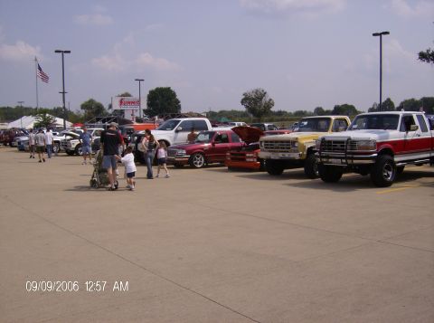 1970 Ford Ranchero - A variety of trucks and cars are parked in a lot, possibly at a car show, under a partly cloudy sky.
