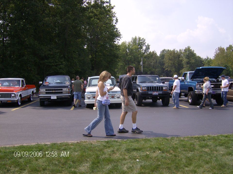 Several pickup trucks and SUVs parked in a lot, some with hoods open. People are walking around