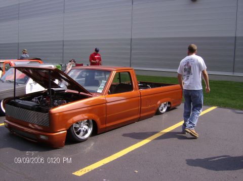 1970 Ford Ranchero - Orange pickup truck with custom grille and lowered suspension, hood open, parked at an outdoor event.