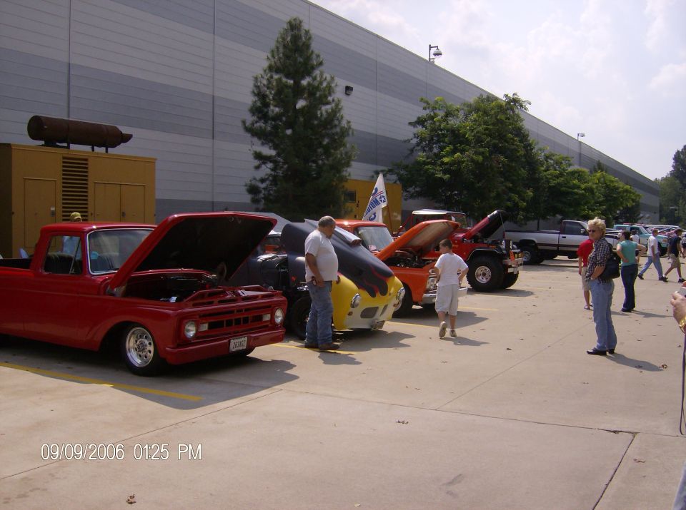 Red 1965 Ford F-100 pickup with hood open, parked in a line with other vehicles