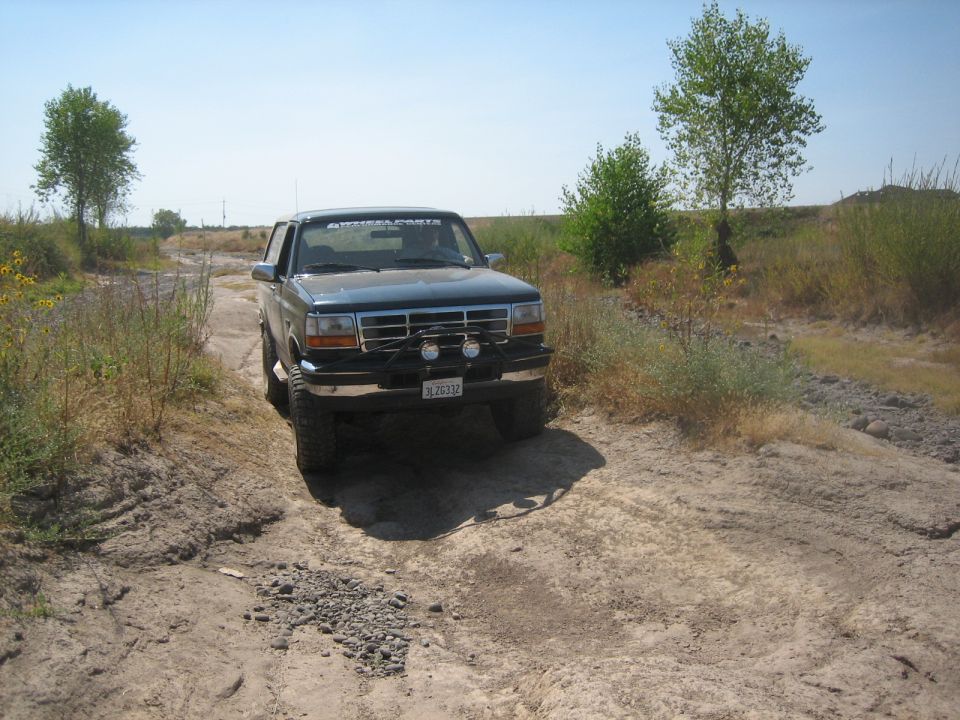 1995 Ford Bronco 3q-front view on dirt road. Dark blue SUV with aftermarket bumper and lights