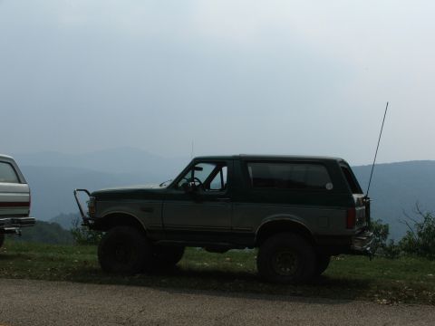 1996 Ford Bronco - A lifted Ford Bronco sits parked on the side of a road with a scenic mountain view.